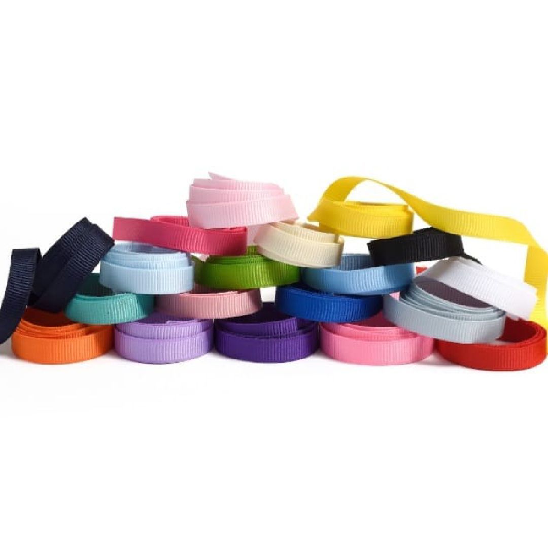 Cintas de grosgrain de colores apiladas y dispuestas de forma desordenada sobre un fondo blanco.