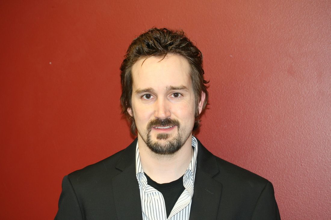 A man in a suit and tie is standing in front of a red wall.