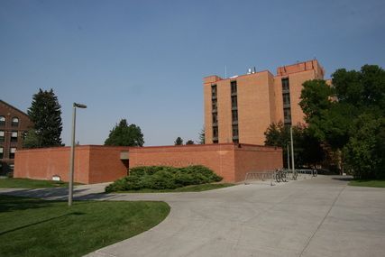 A large brick building with a lot of windows is surrounded by trees and grass.