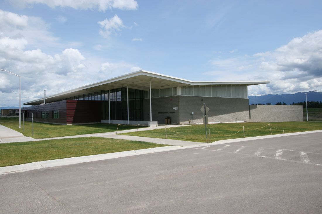 A large building with a roof that is covered in shingles is sitting on top of a lush green field.