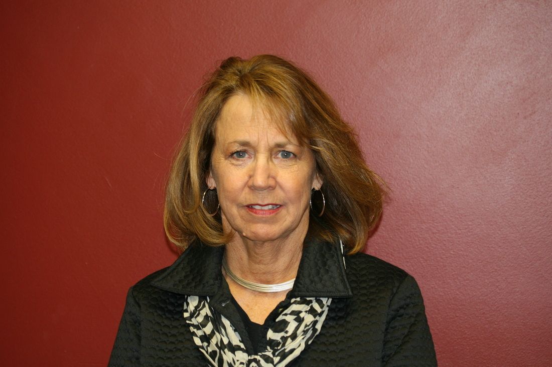 A woman in a black shirt and scarf is standing in front of a red wall.
