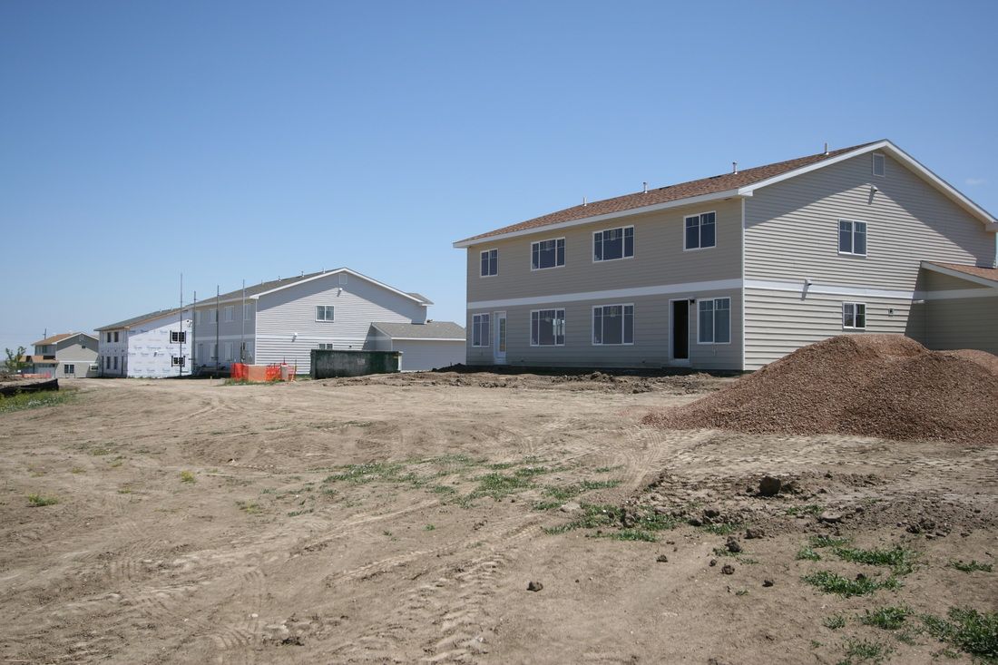 A group of houses are being built in a dirt field.