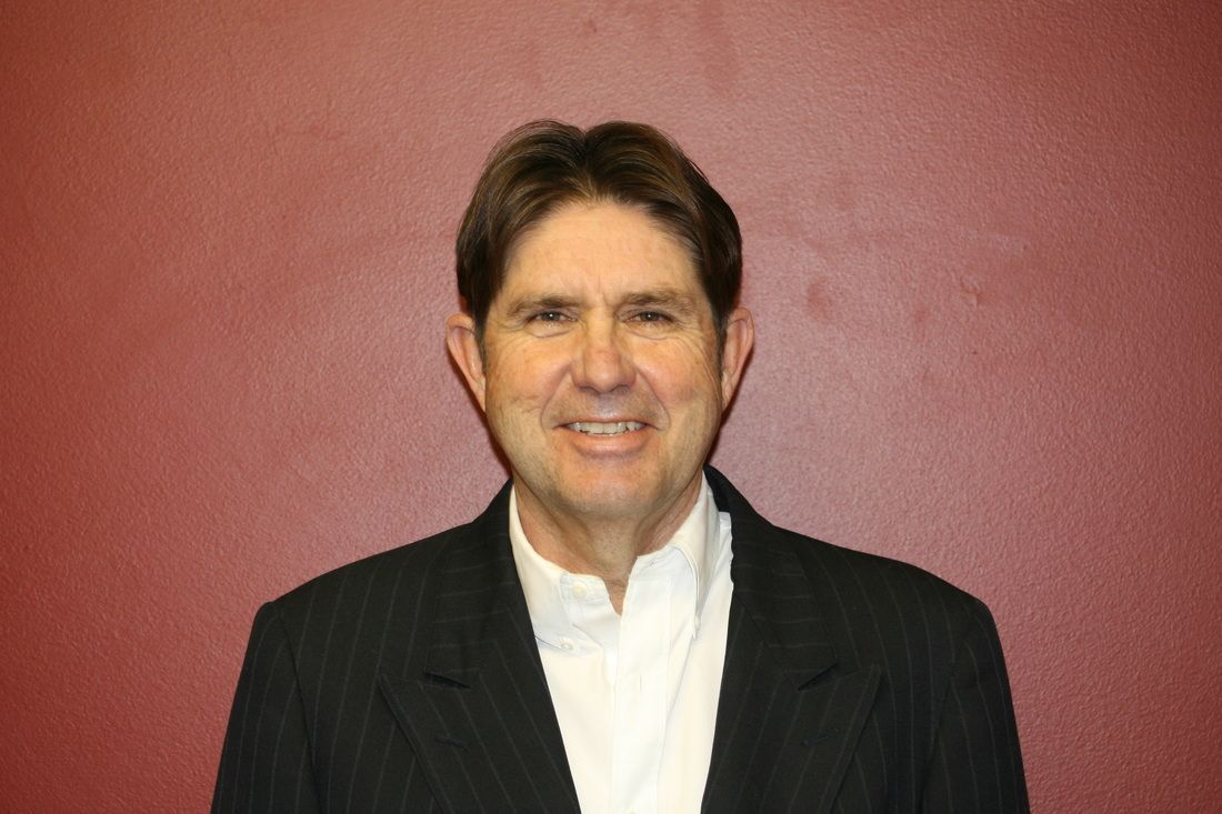 A man in a suit and white shirt is smiling in front of a red wall.