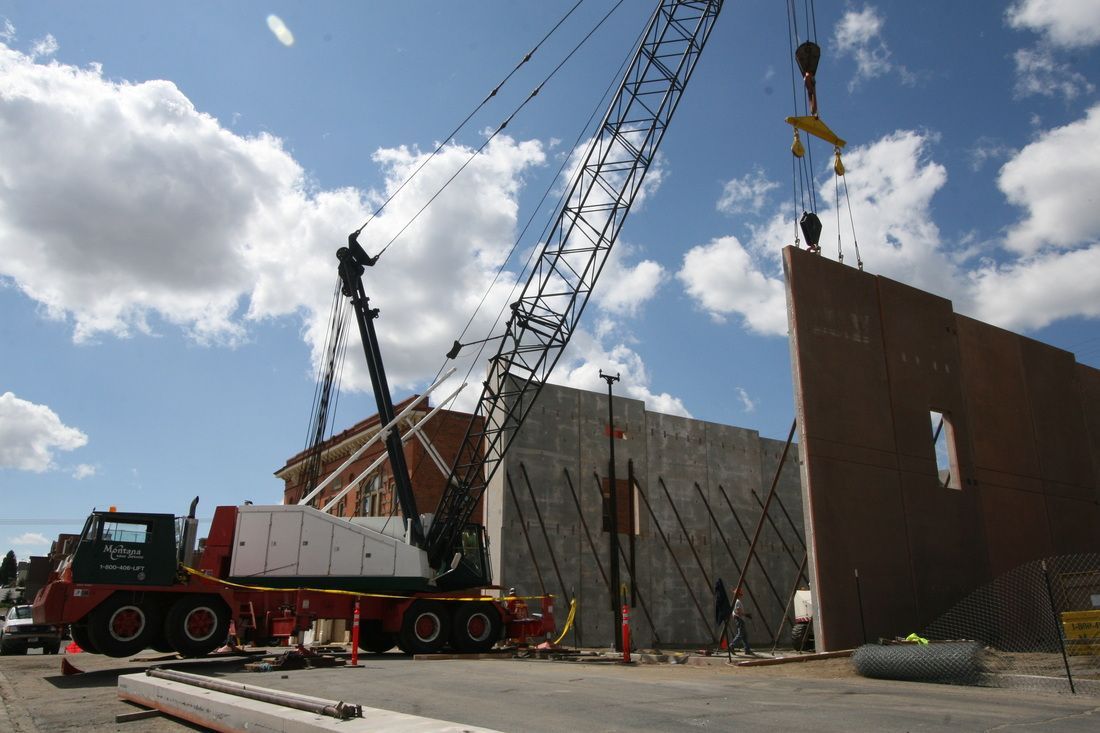 A crane is lifting a piece of concrete in front of a building under construction