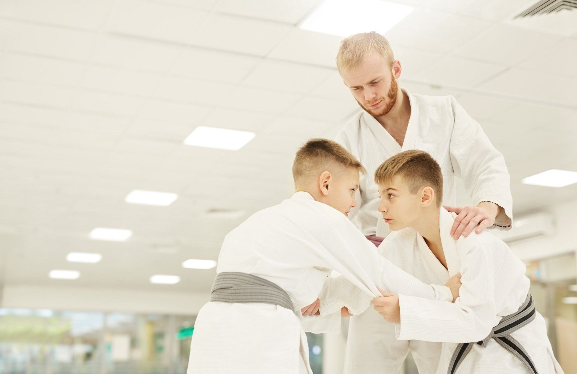 Three martial arts students and instructor in white uniforms practicing together indoors