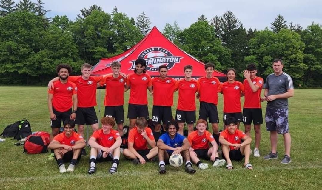 Soccer team posing in red jerseys in front of a red tent on a grassy field, with trees in the background