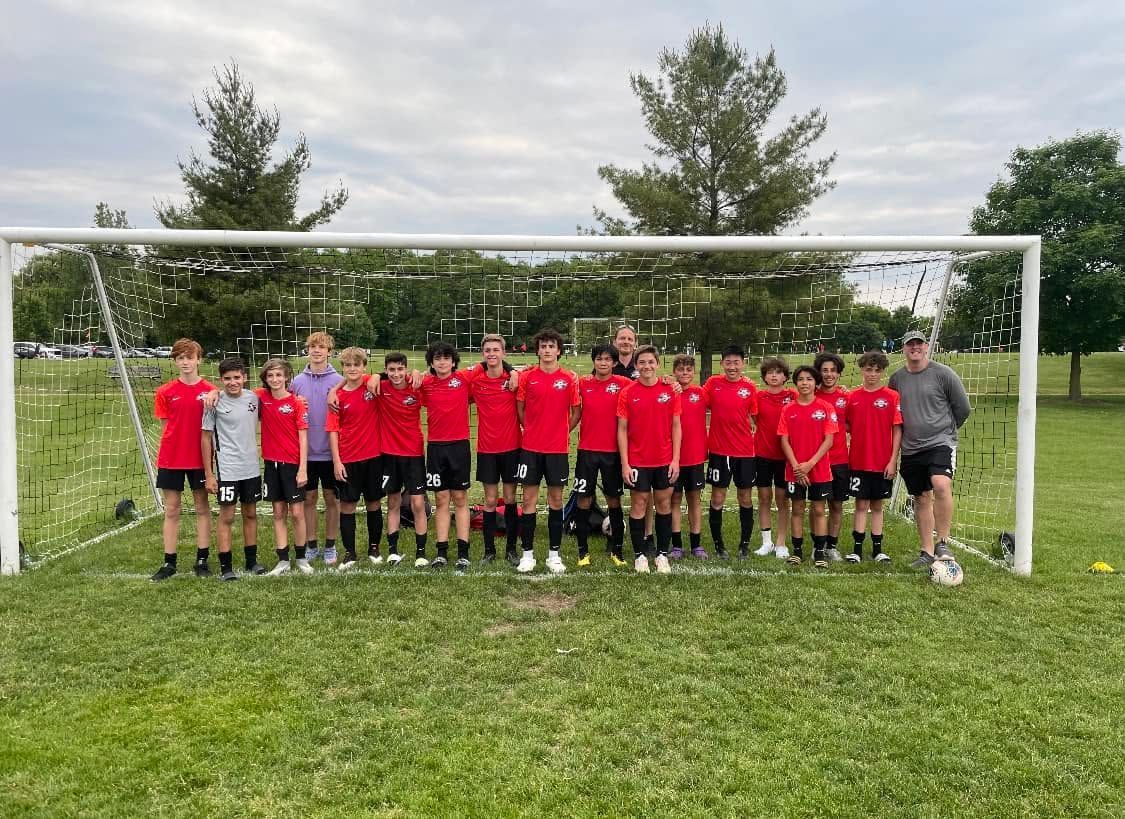 Youth soccer team in red jerseys posing in front of a goal on a grassy field.