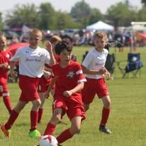 Youth soccer players in red and white uniforms chasing the ball on a grassy field