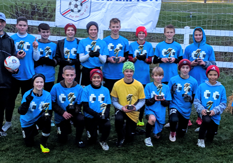Youth soccer team posing in blue jerseys on a wet field, with a banner behind them