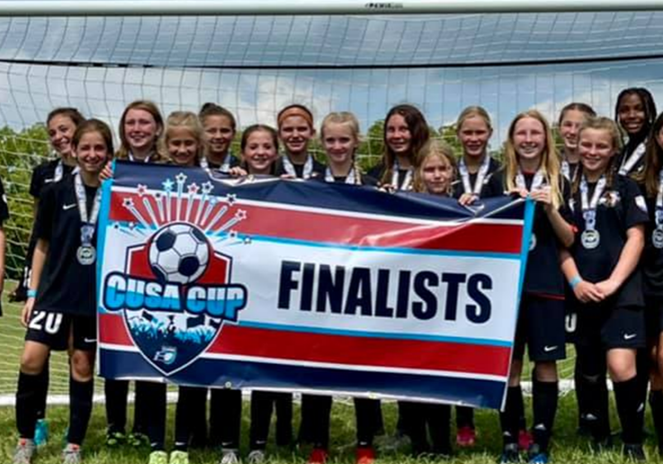 Youth soccer team holding a “FINALS” banner on a field with medals around their necks