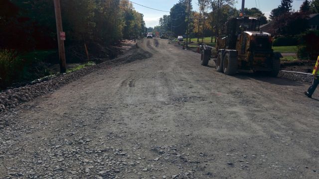 A man is walking down a dirt road next to a bulldozer.
