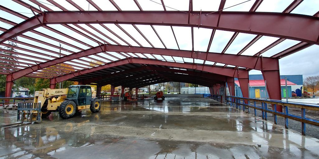 A yellow tractor is parked under a red metal structure.