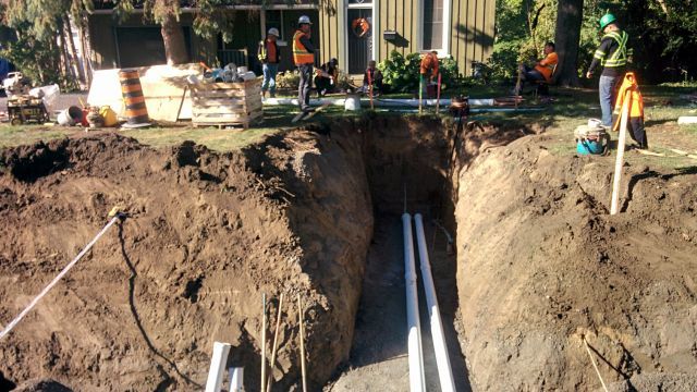 A group of construction workers are digging a hole in the ground in front of a house.