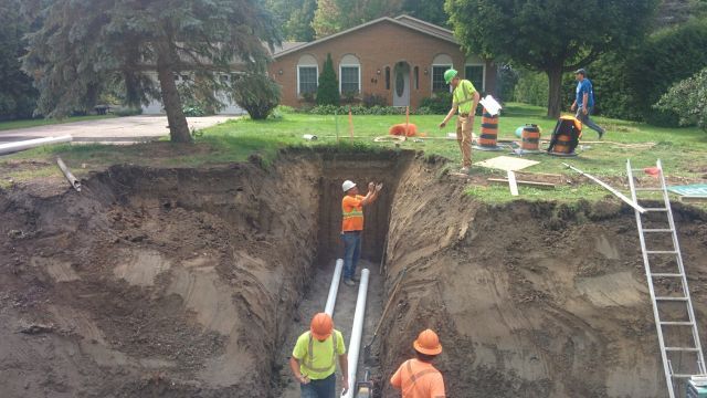 A group of construction workers are working in a trench in front of a house.