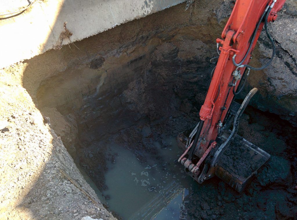 A red excavator is digging a hole in the ground.