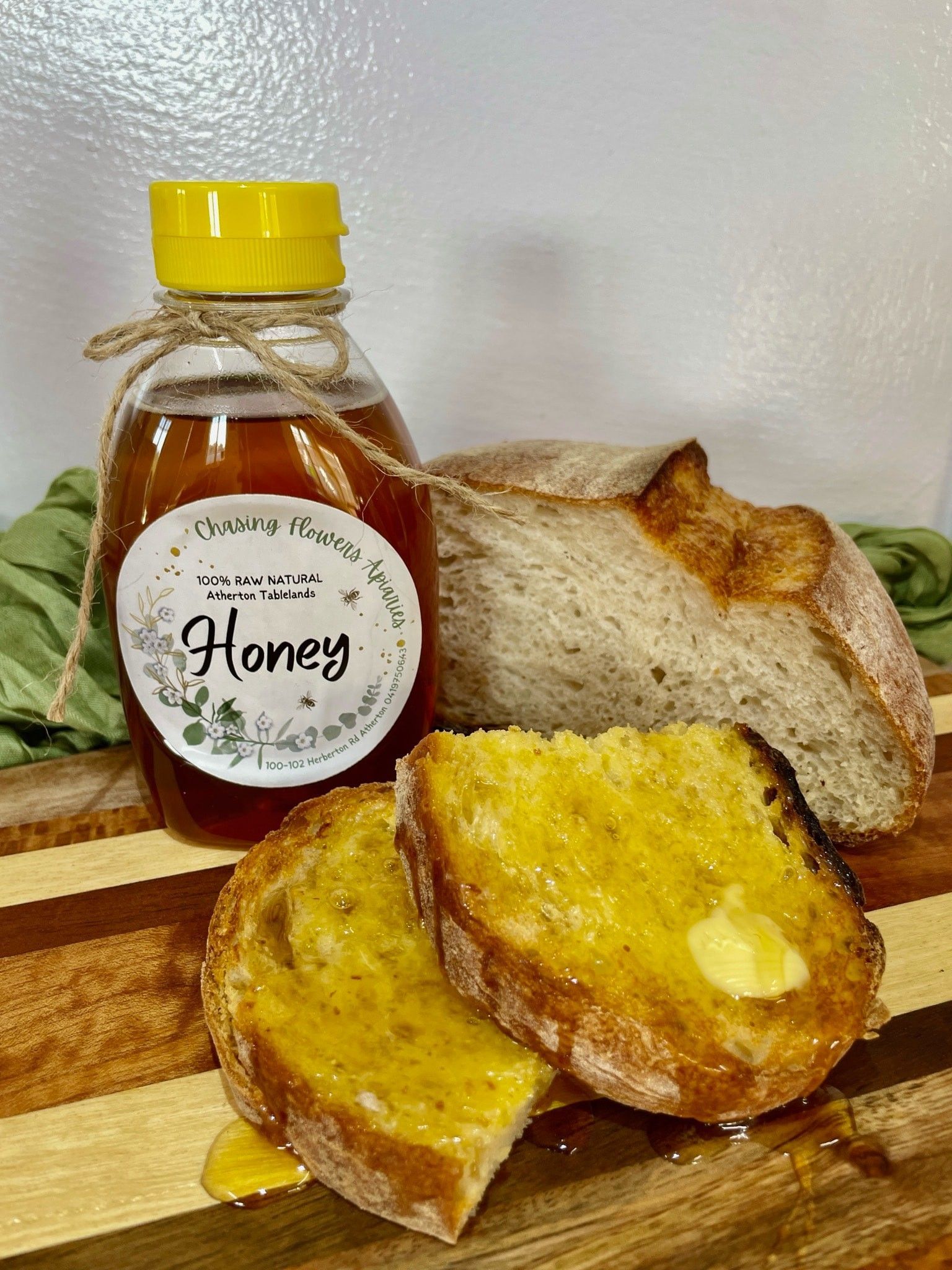 Honey bottle, rustic bread, and two slices of toast with melting butter on a wooden cutting board.