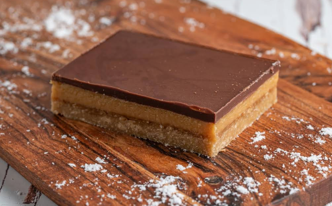Chocolate caramel slice on a wooden board, dusted with powdered sugar.— Atherton Bakehouse in Atherton, QLD