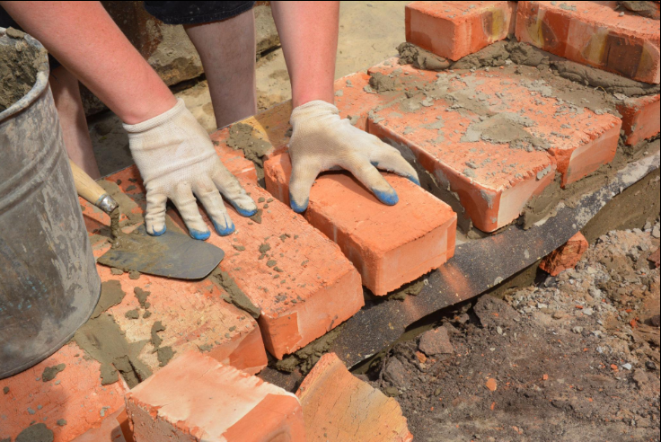 “Worker carefully setting red bricks into fresh mortar for a sturdy brick wall during a masonry service in Pearland, TX”