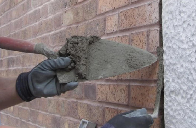 “Close-up of a trowel spreading fresh mortar onto a brick wall joint during a masonry service in Pearland, TX”