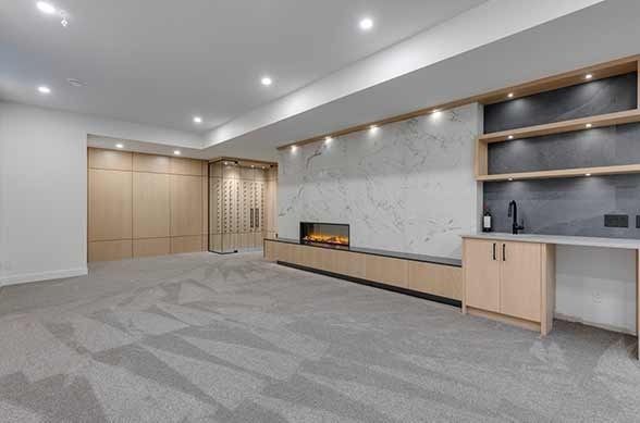 Modern kitchen with light wood floor, island with bar stools, brown cabinets, and overhead pendant lights.