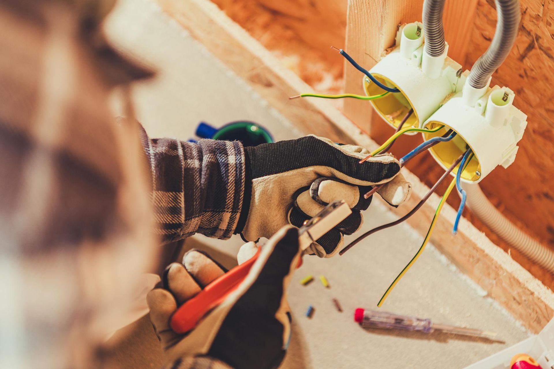 Electrician wiring electrical outlets, wearing work gloves, with exposed wires.