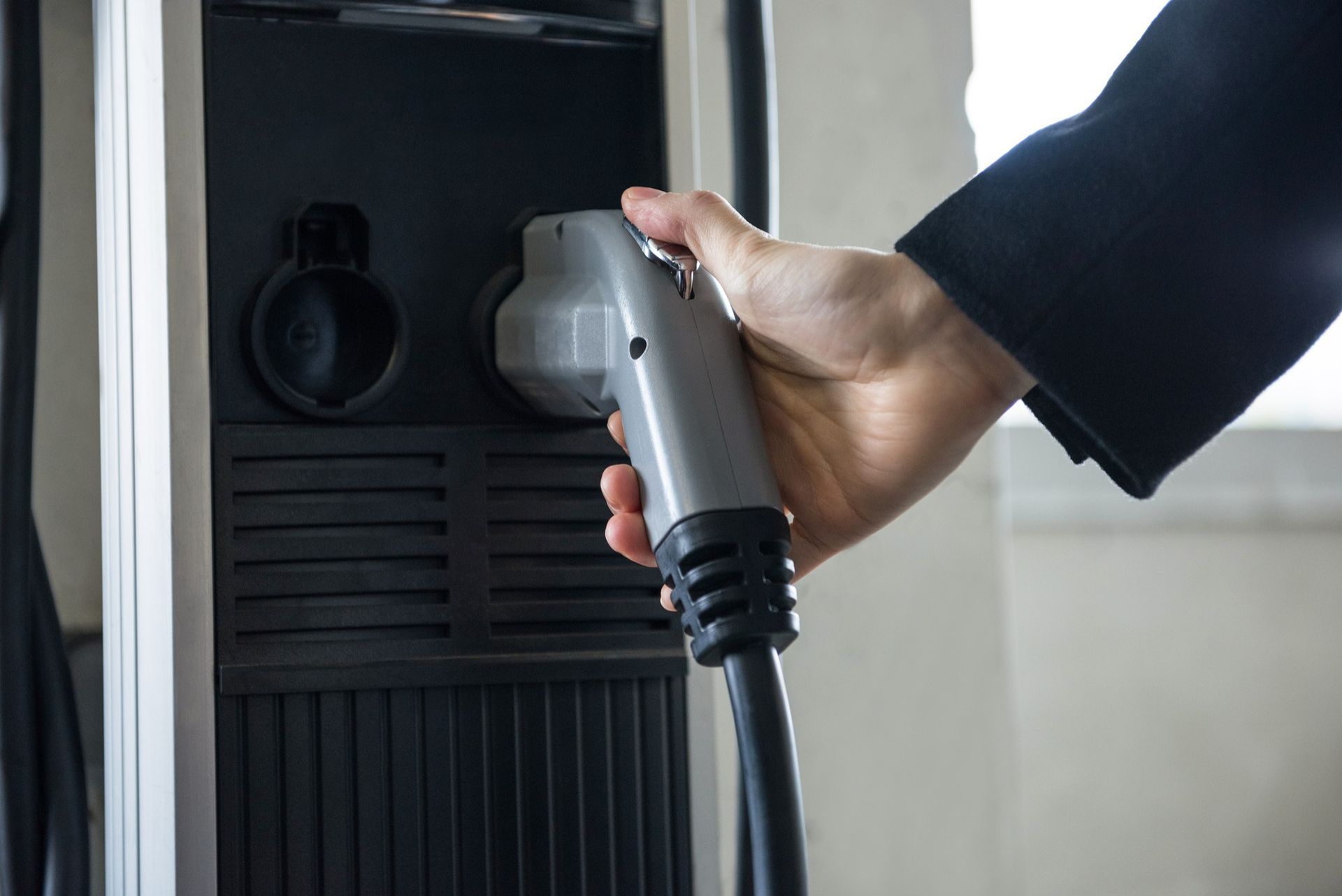 Hand plugging a gray charging cable into an electric vehicle charging station.