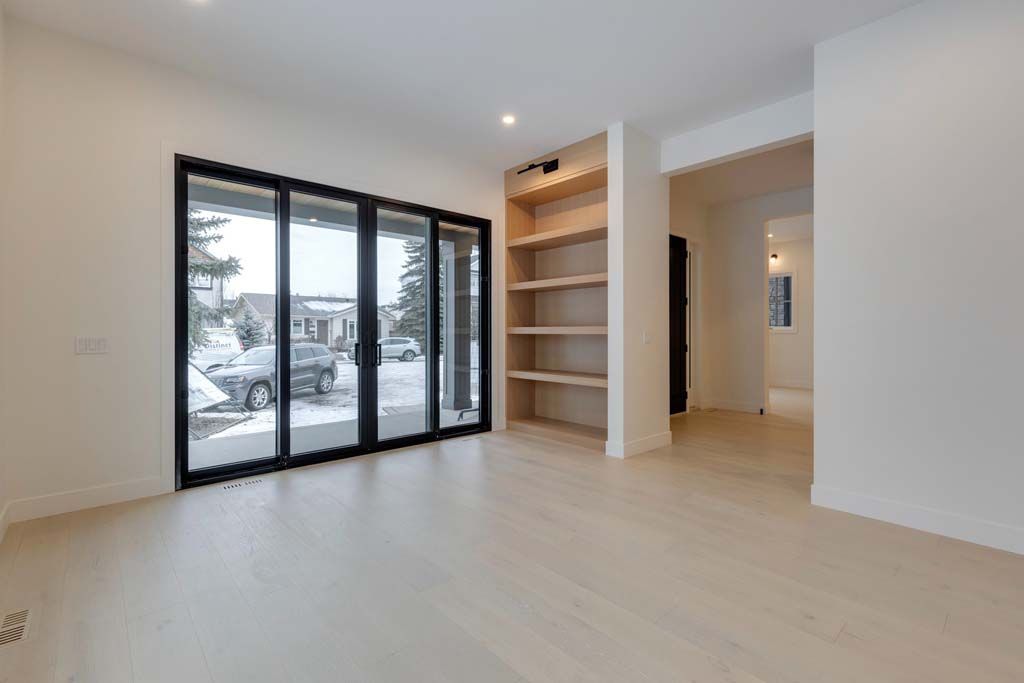 Empty room with sliding glass doors, built-in shelving, and light wood floors. Snow outside the doors.