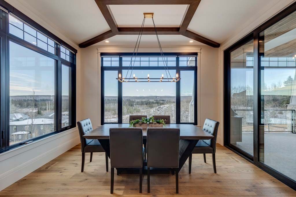 Dining room with large windows, wooden table and chairs, and a chandelier.