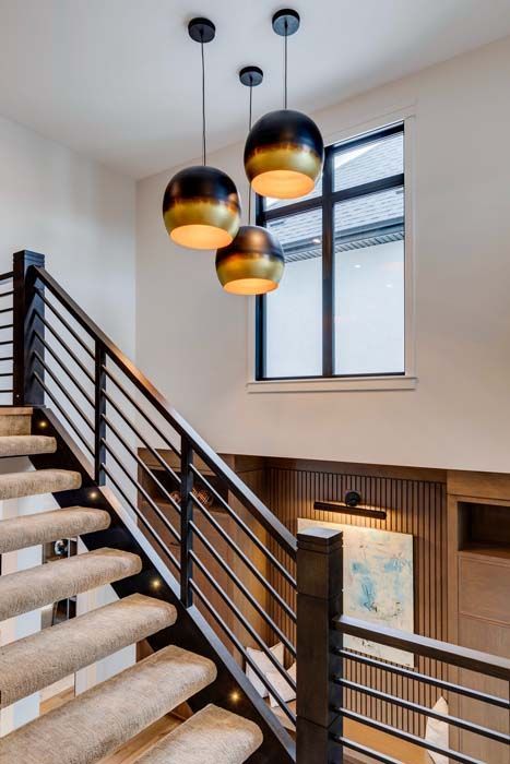 Staircase with black metal railings, carpeted steps, and three hanging black and gold pendant lights.