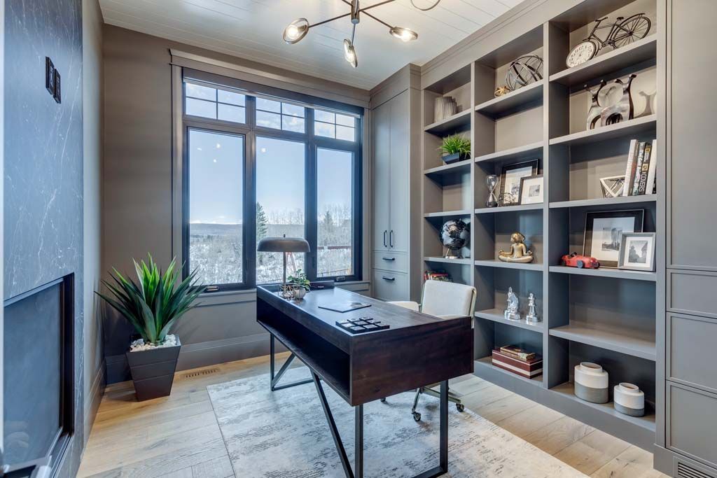 Home office with dark gray walls, built-in shelves, a desk, and a large window.
