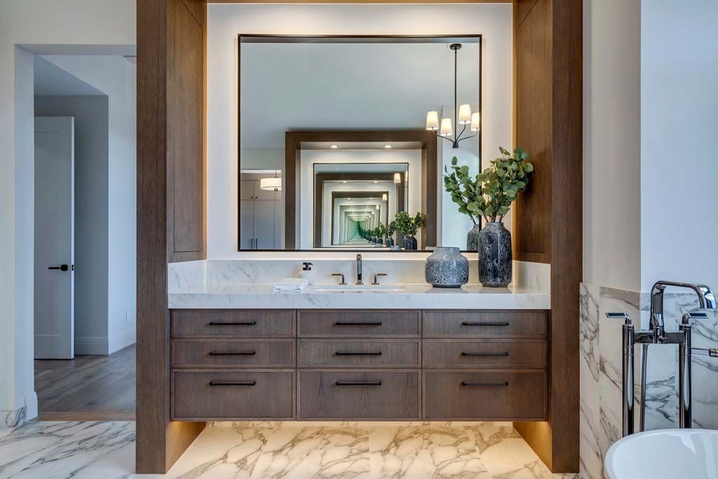 Bathroom vanity with large mirror, dark wood, white marble countertop, and decorative vases.