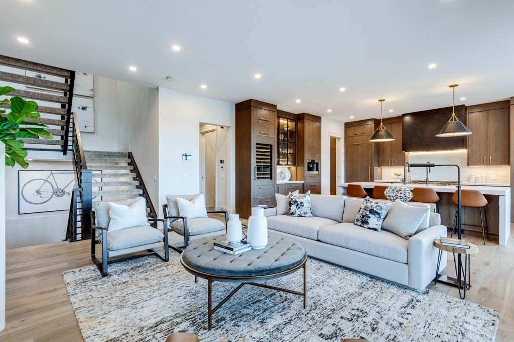 Modern living room with open kitchen, light wood floors, and neutral furnishings.