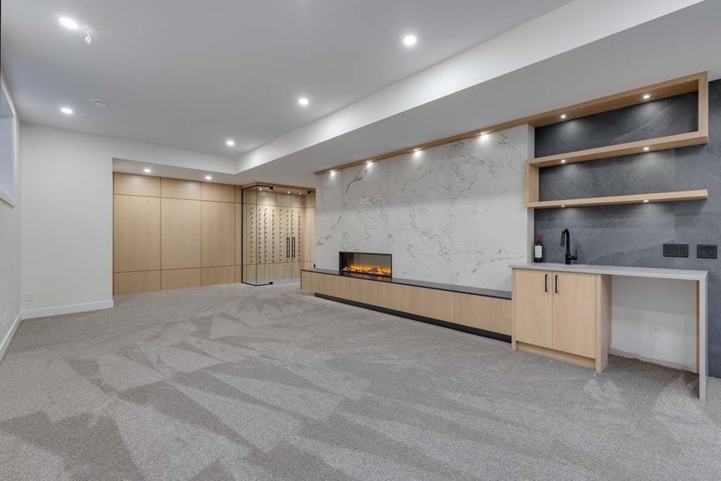 Spacious, modern basement with neutral carpet, built-in bar, fireplace, and cabinets.