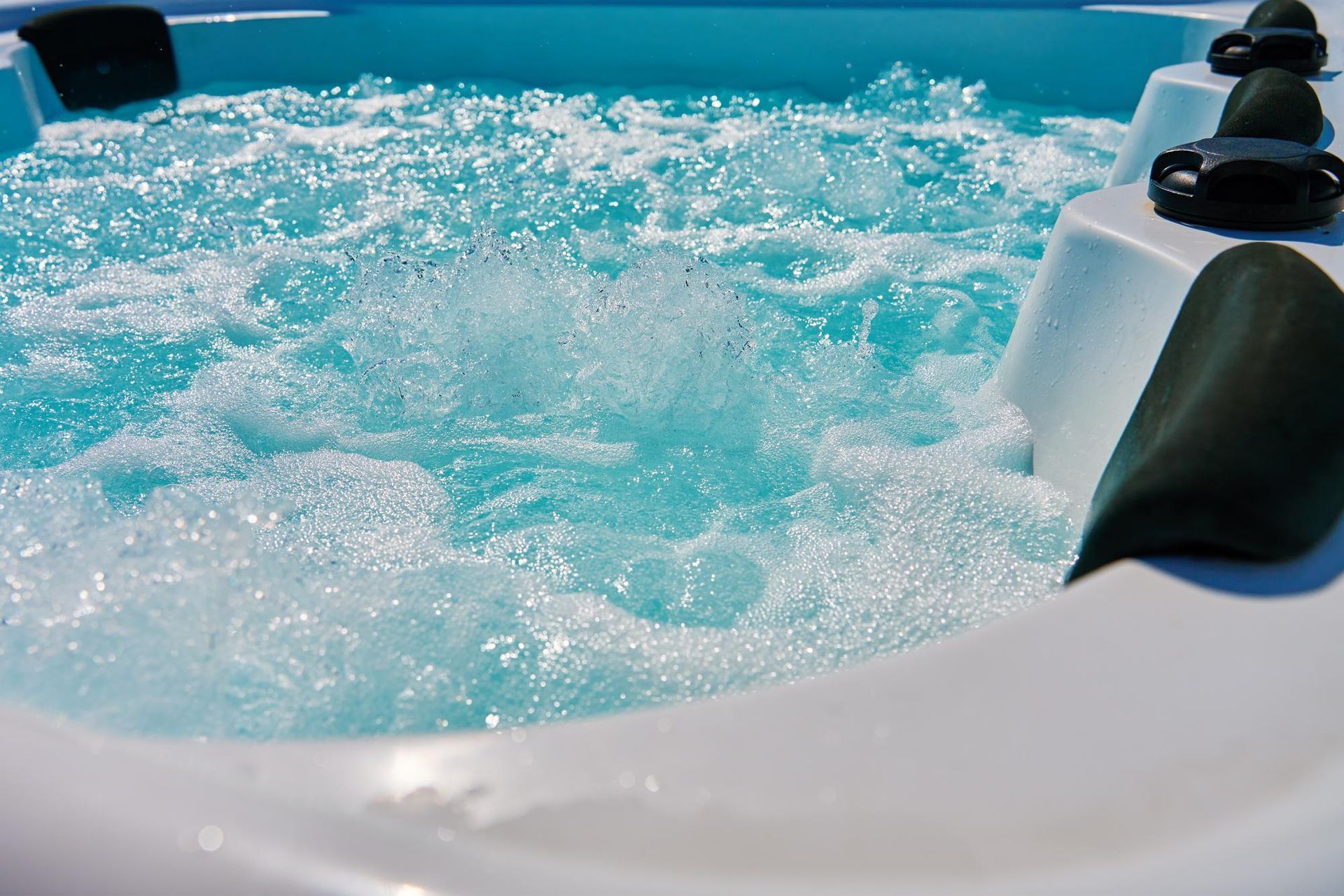 Bubbling turquoise water in a white hot tub, jets creating foam.