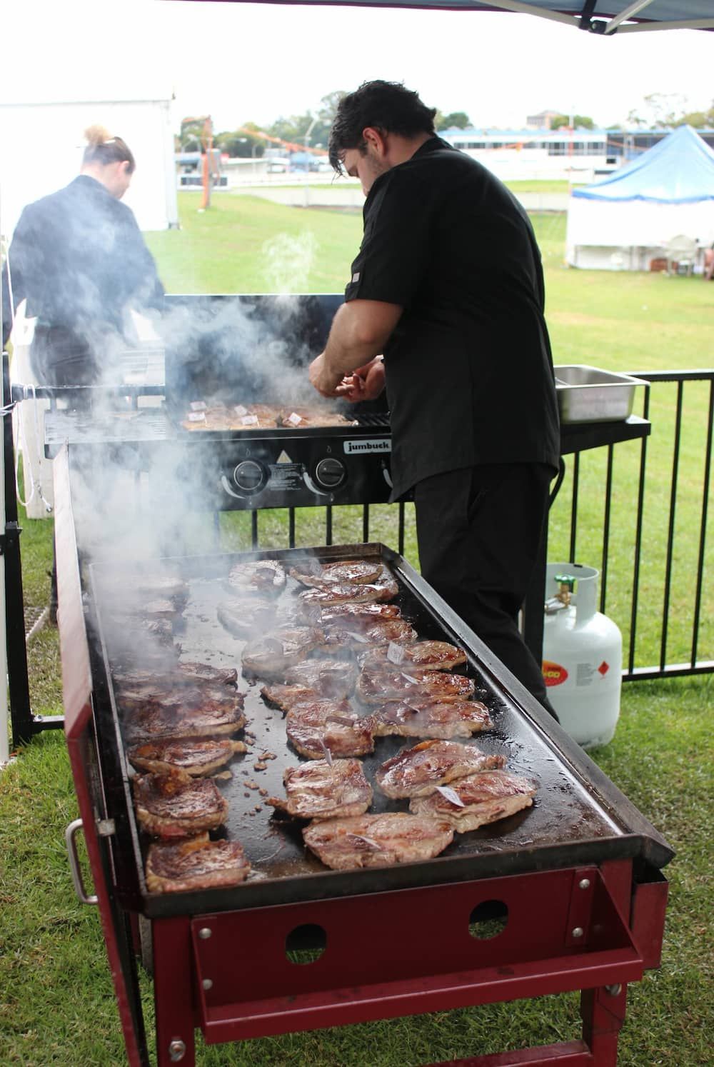 A Man Is Cooking Steaks On A Grill Outside — Vines at 139 in Grafton, NSW