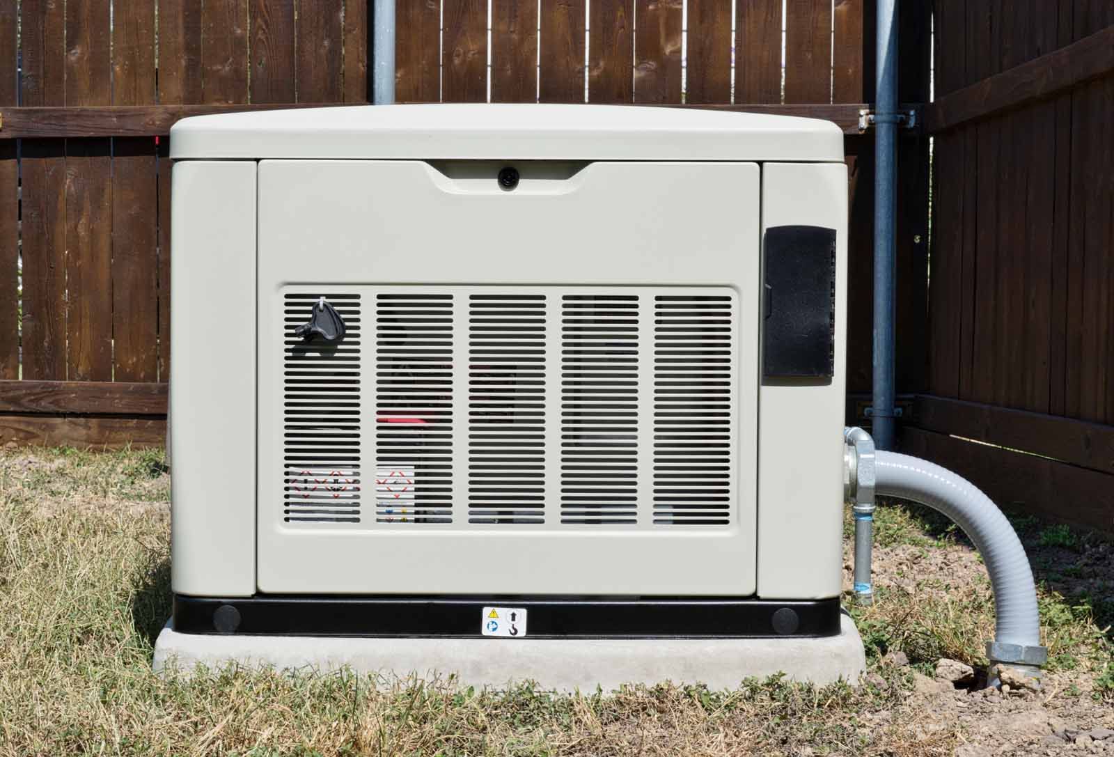 A generator is sitting in the grass next to a wooden fence.
