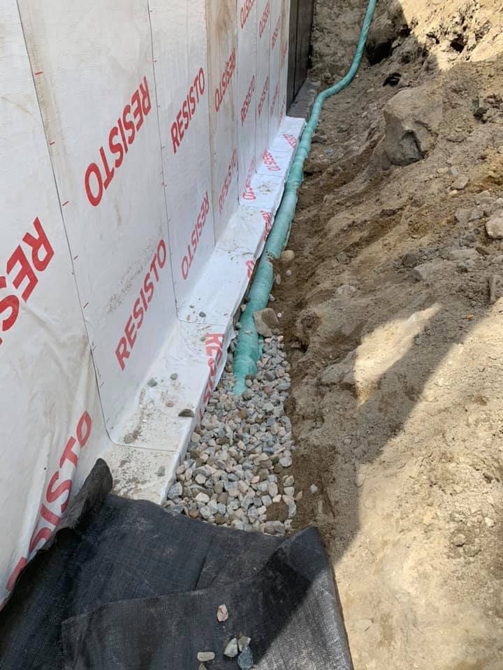 Tuyau de drainage vert installé le long d'une fondation avec géotextile et gravier.