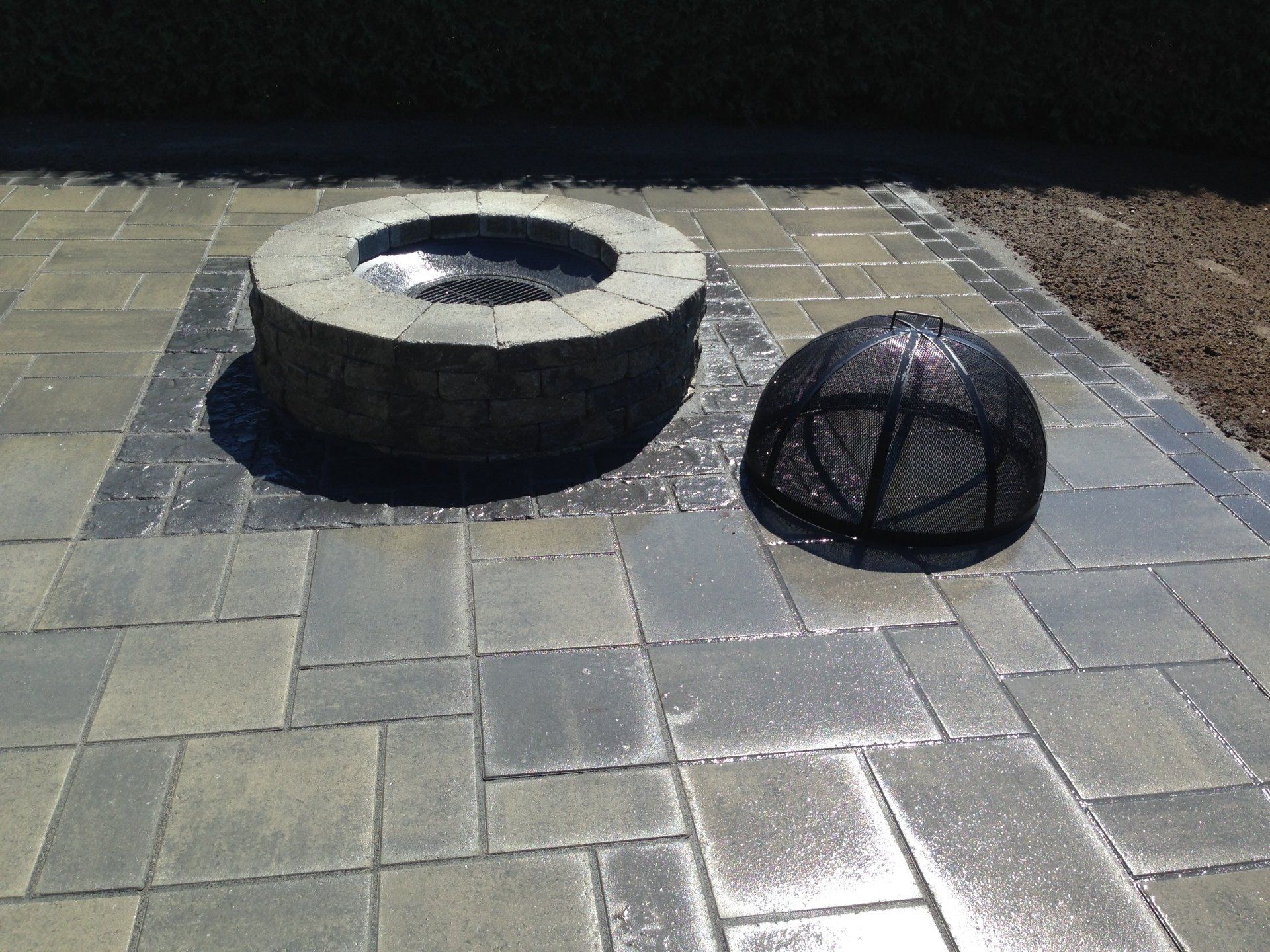 Foyer ext&eacute;rieur circulaire en pierre avec grille de protection sur pav&eacute;s rectangulaires.
