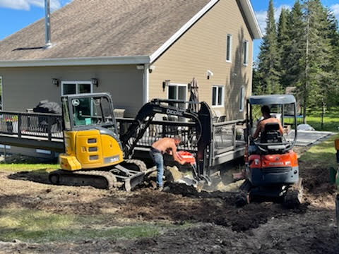 Excavatrice et équipements de construction près d'une maison résidentielle avec terrain en préparation.