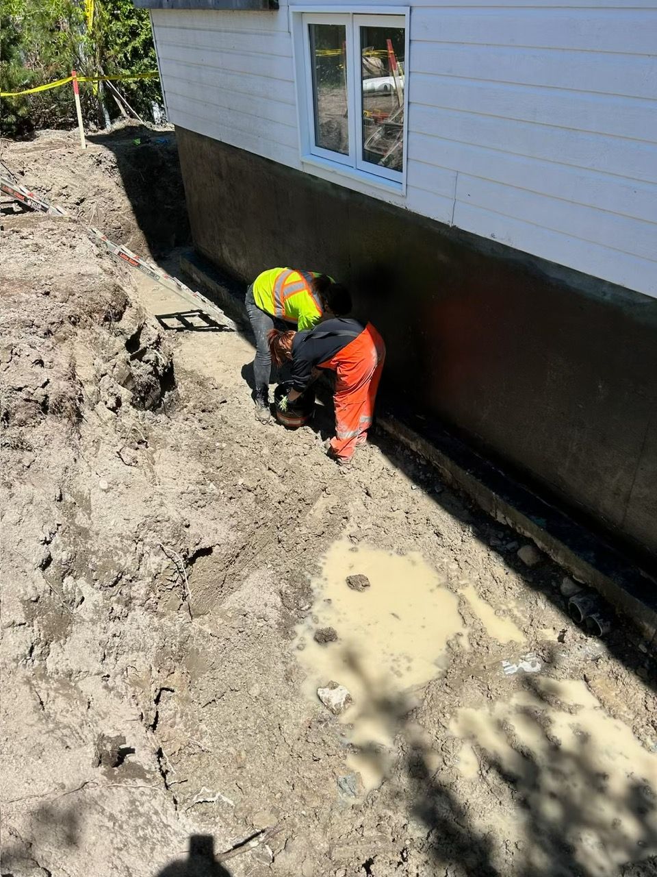 Ouvrier en vêtements de sécurité travaillant dans une tranchée contre la fondation d'une maison.