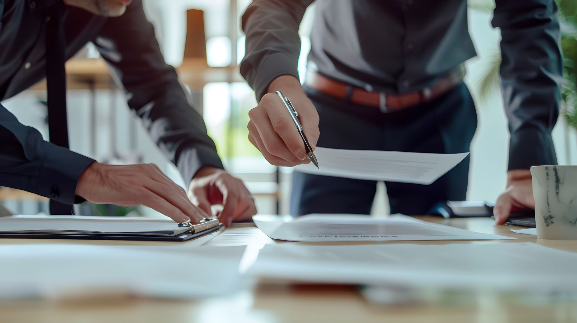 Two people in dark shirts reviewing documents at a desk, one points with a pen.