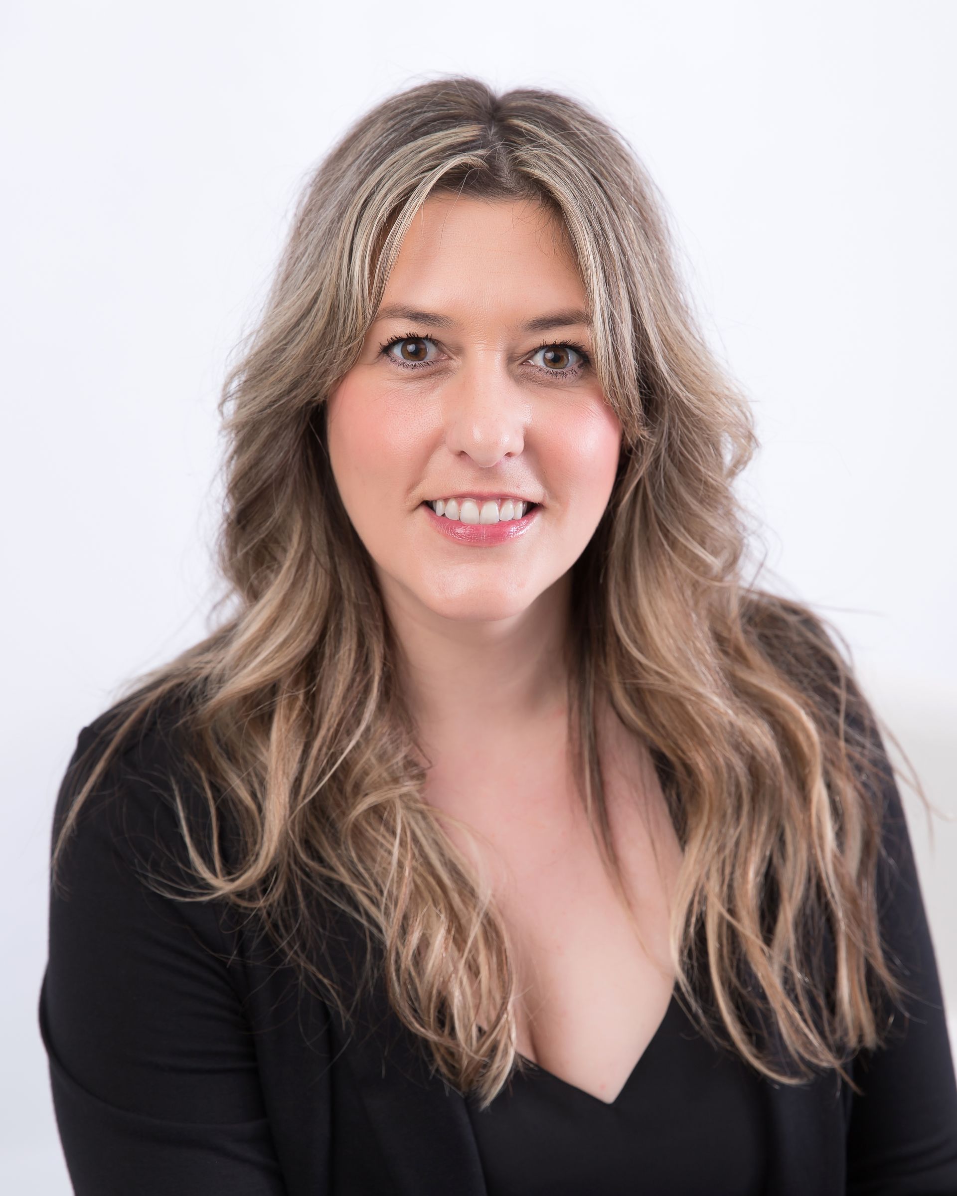 Woman with long wavy hair smiles, wearing a black top against a white background.