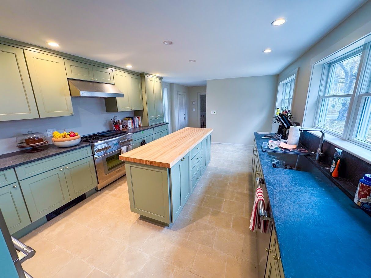 Bright kitchen with green cabinets, wood island, and blue countertop beside a windowed sink.