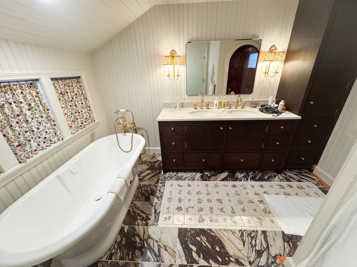Bright bathroom with clawfoot tub, dark wood vanity, marble-look floor, and gold wall sconces.