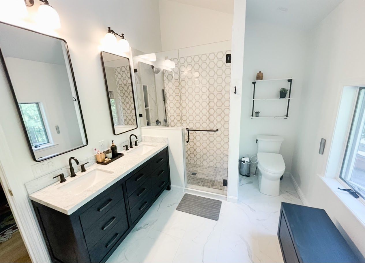 Bright white bathroom with black vanity, large mirrors, tiled shower, and toilet near a window.