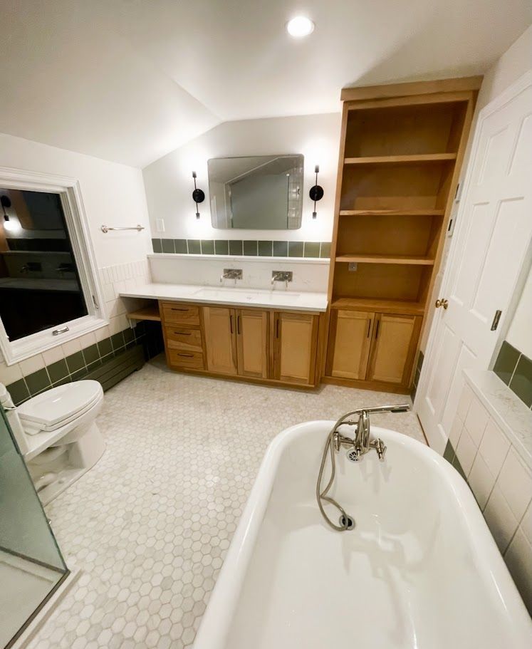 White bathroom with clawfoot tub, double vanity, mirror, toilet, and built-in shelves on the right.