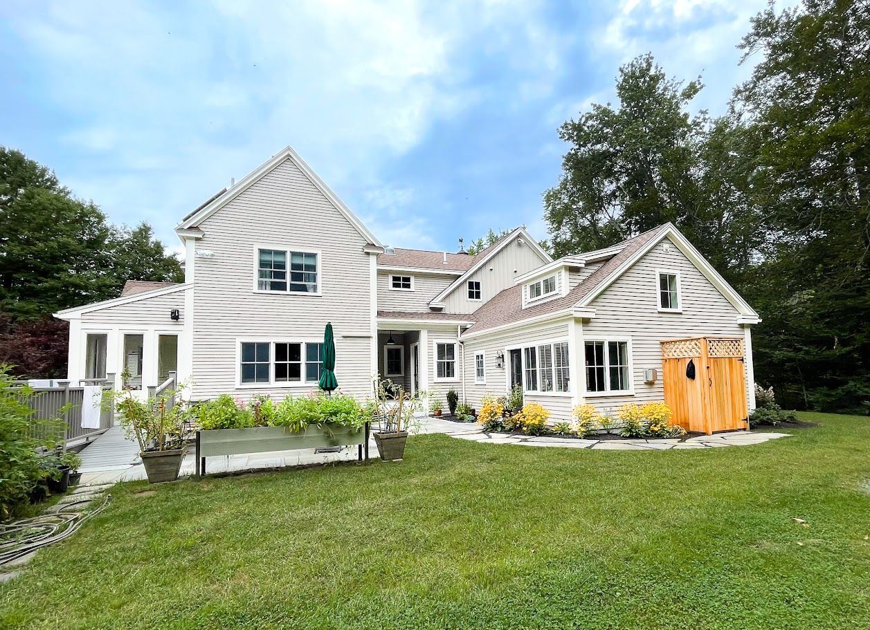 White house with gabled roof and garden, set on a grassy lawn under a blue sky.