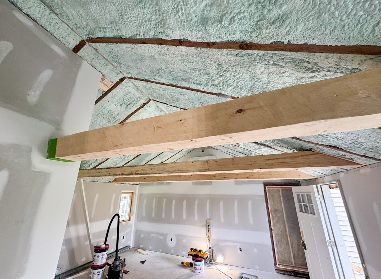 Unfinished room ceiling with exposed wooden beams and insulation, drywall partially installed below.