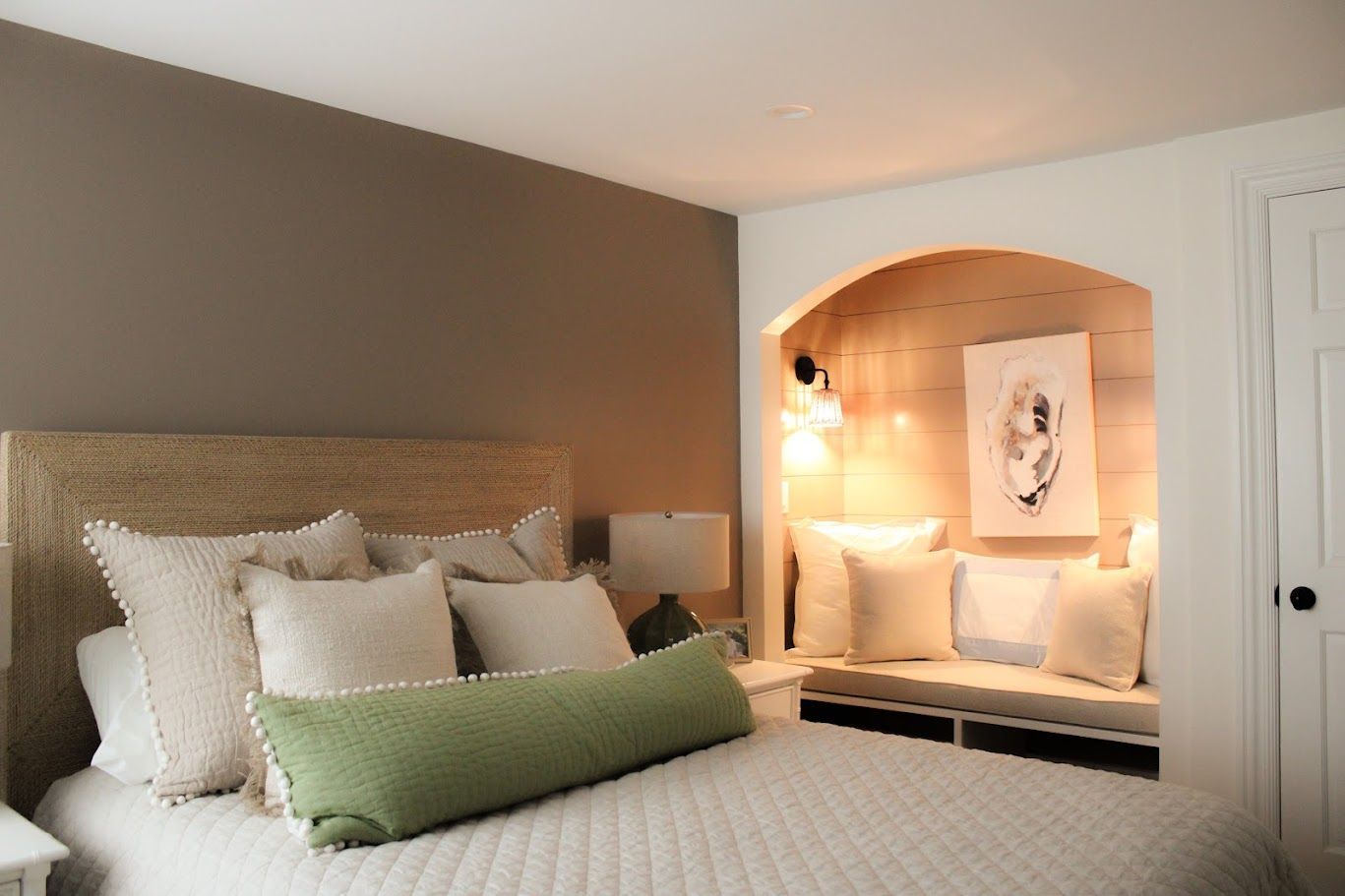 Cozy bedroom with woven headboard, green lumbar pillow, and lit alcove reading nook