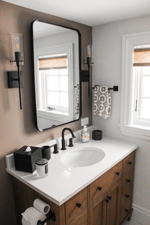 Modern bathroom vanity with round sink, black fixtures, wood cabinet, and large mirror by two windows